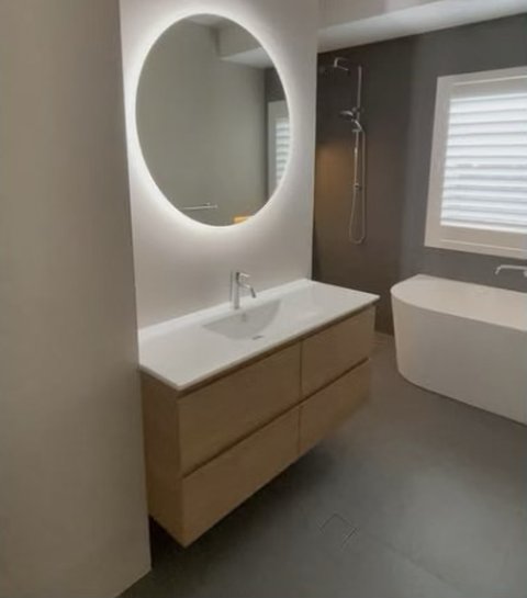 Finished bathroom with backlit round mirror, timber vanity and freestanding bath